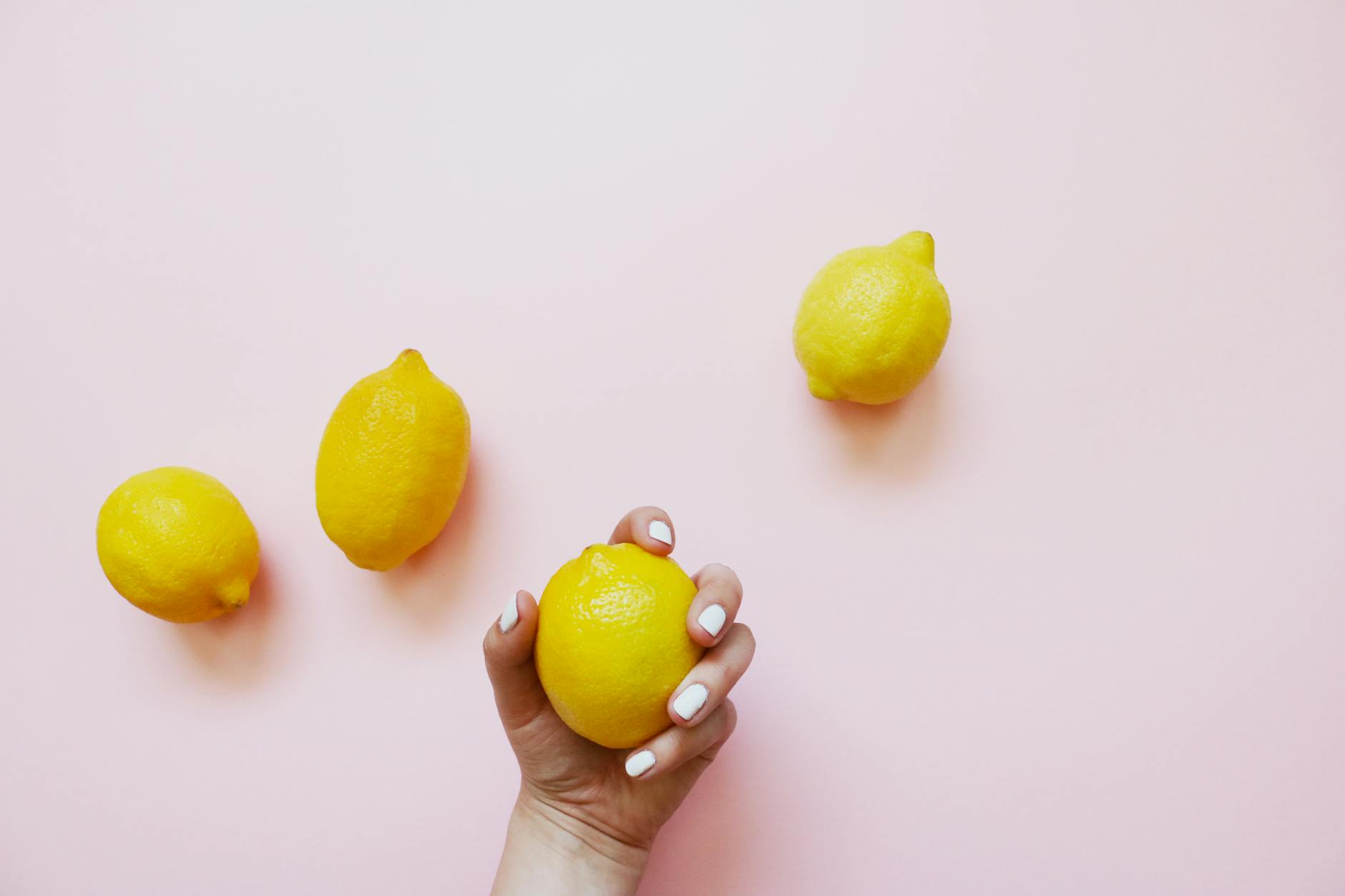 A hand holding a fresh lemon on a soft pink background, symbolizing gentle touch and sensation