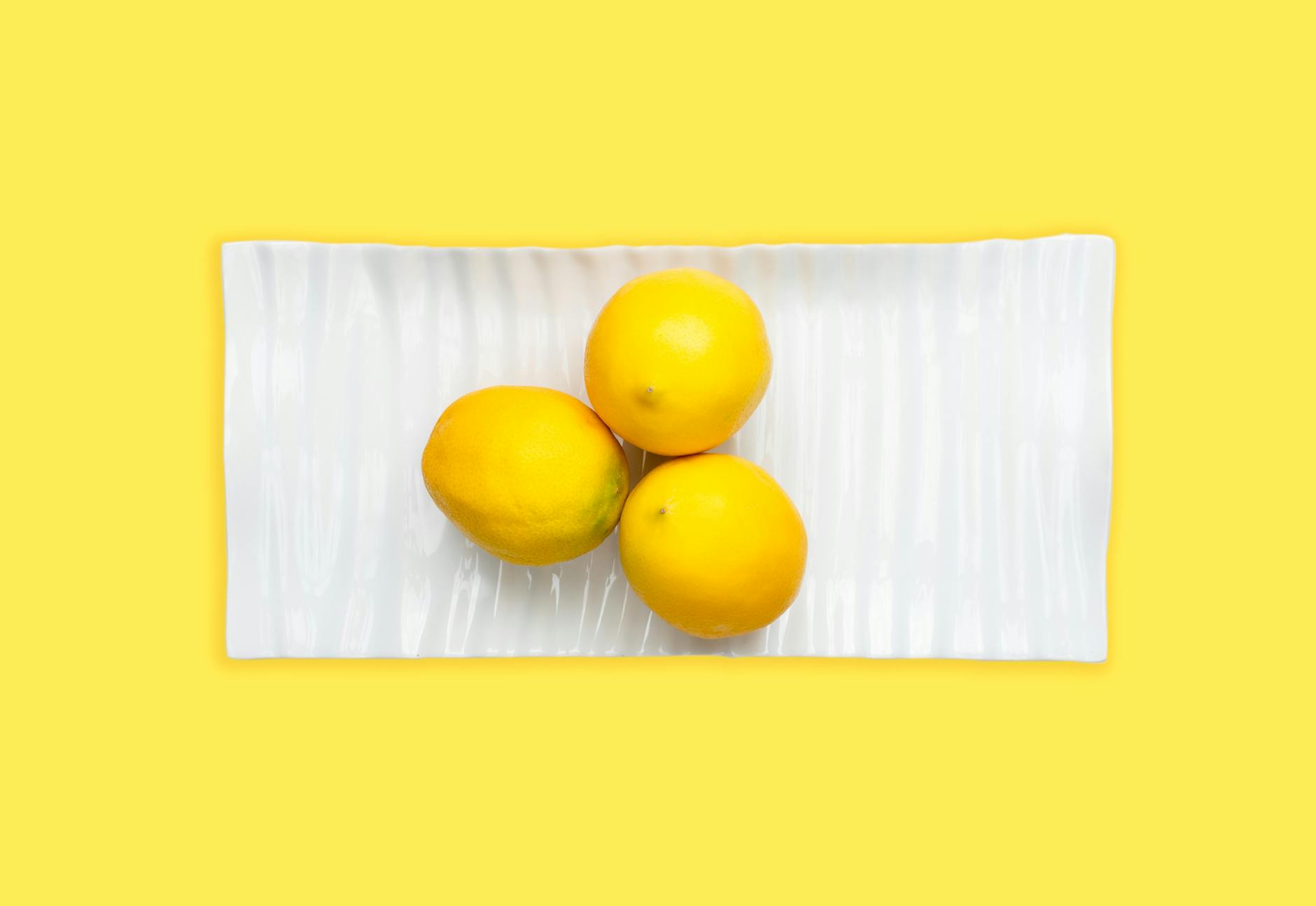 Fresh lemons arranged on a white plate with yellow background, symbolizing fresh starts and bright new beginnings