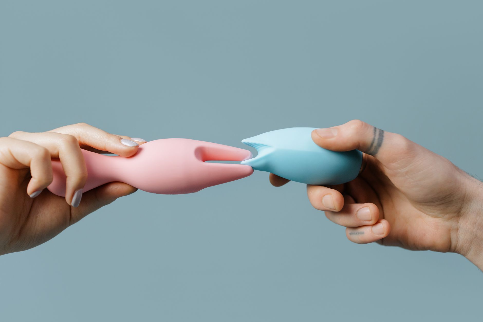 Hands holding colorful silicone adult toys on a soft pastel background