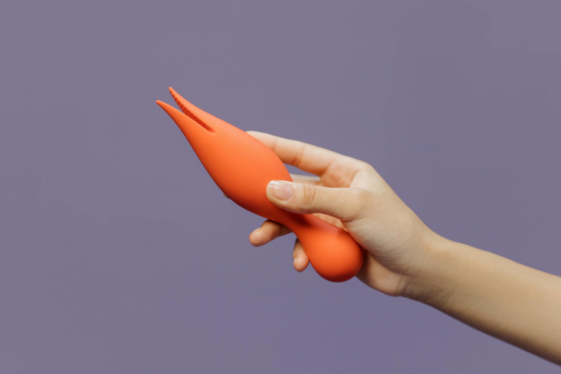 A hand holding a Lemon Clit Sucker vibrator against a minimalist purple background, illustrating modern clitoral pleasure.