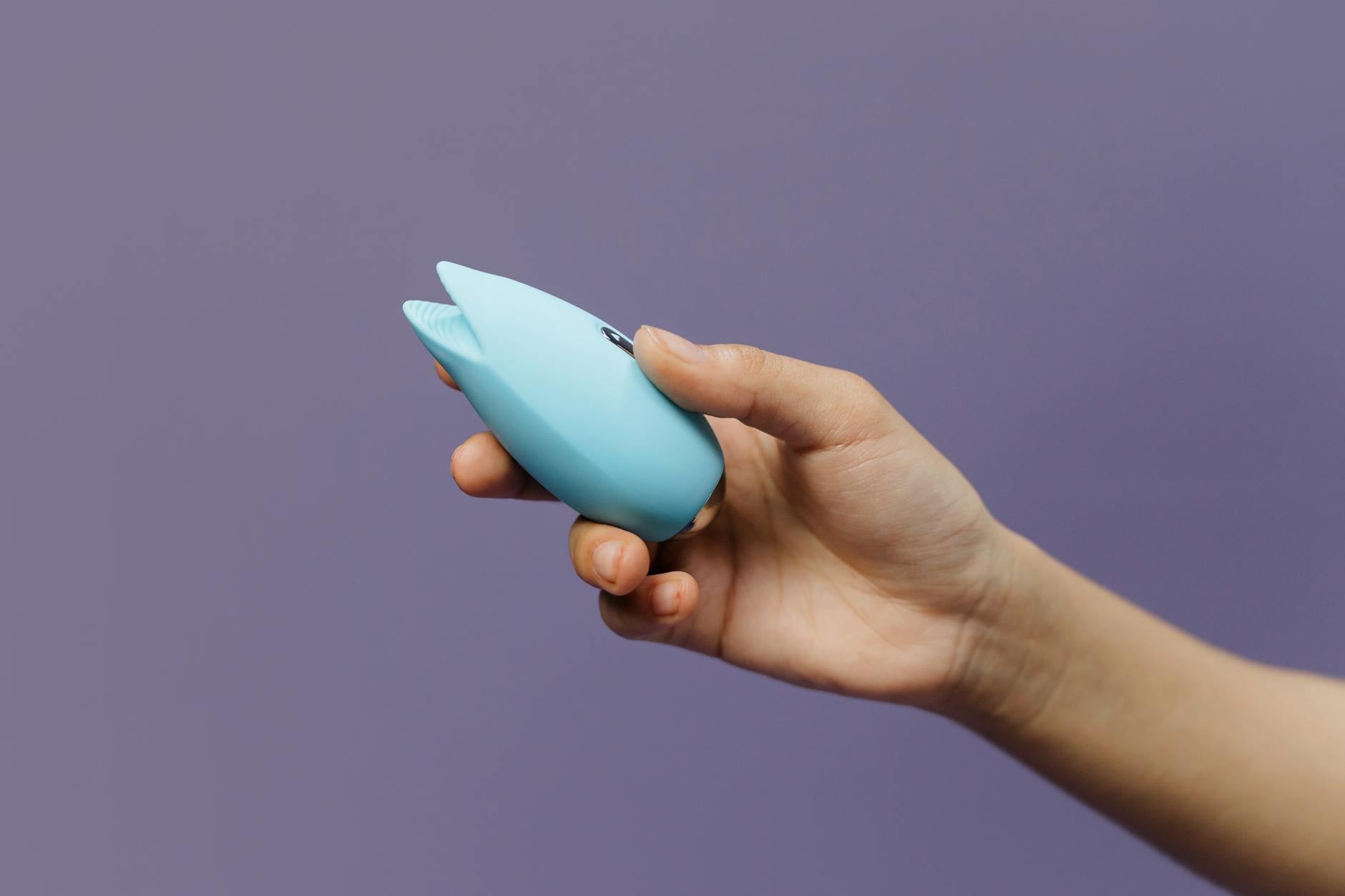 A blue silicone clitoral vibrator held in hand, demonstrating intimate self-care and sexual wellness