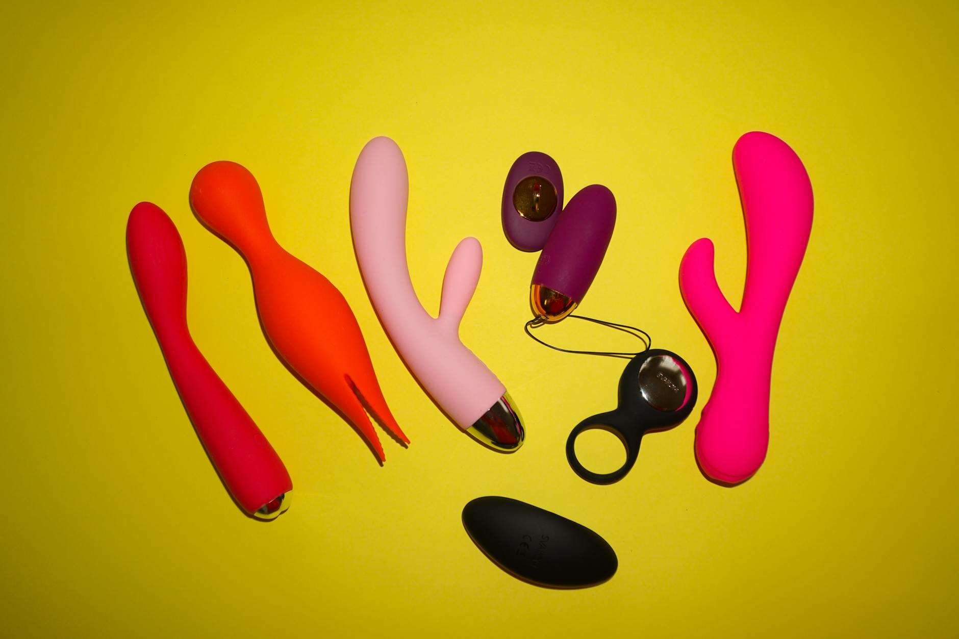 Woman holding blue and pink silicone vibrators with a thoughtful expression