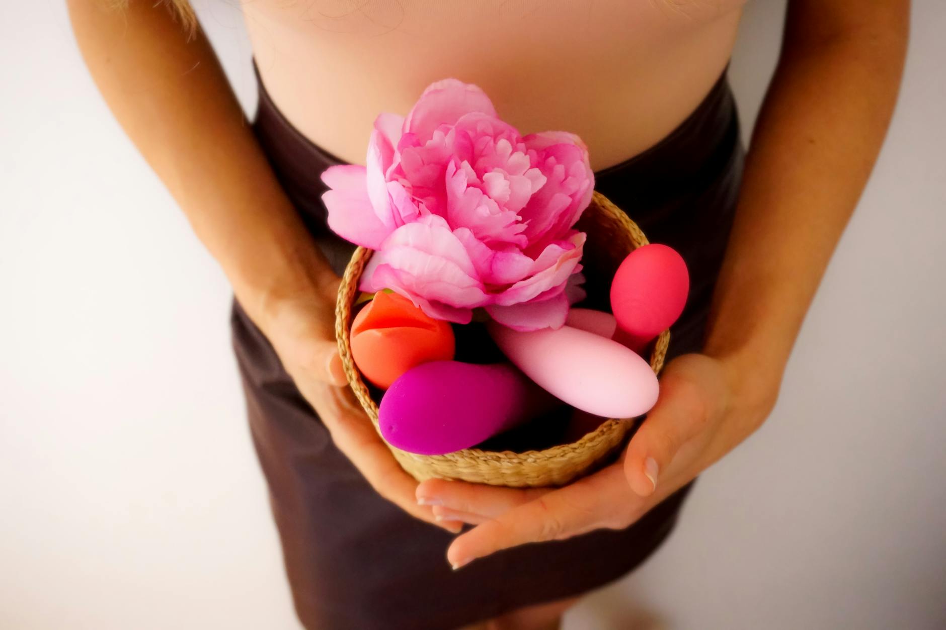 Two hands holding pink and blue silicone vibrators against a pastel background